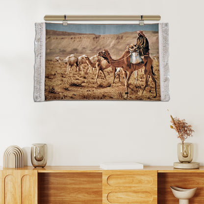 Wall tapestry depicting Bedouin man riding a camel across the desert with camel herd, in warm earthy tones